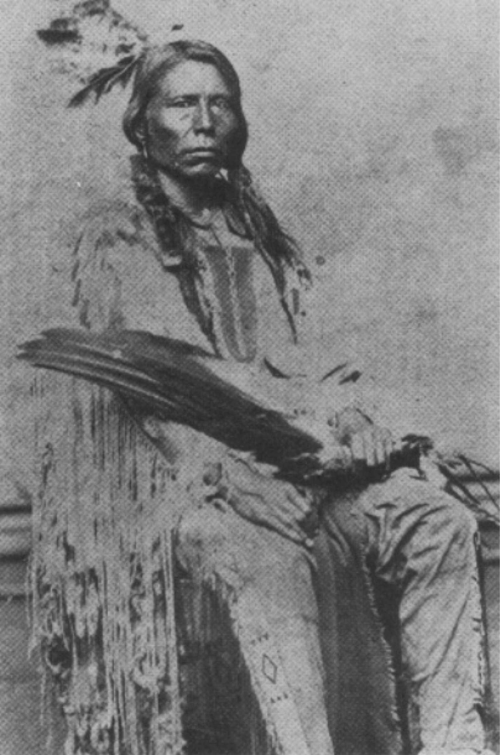 the man named Crazy Horse, sitting, he has long hair, and is wearing traditional dress.